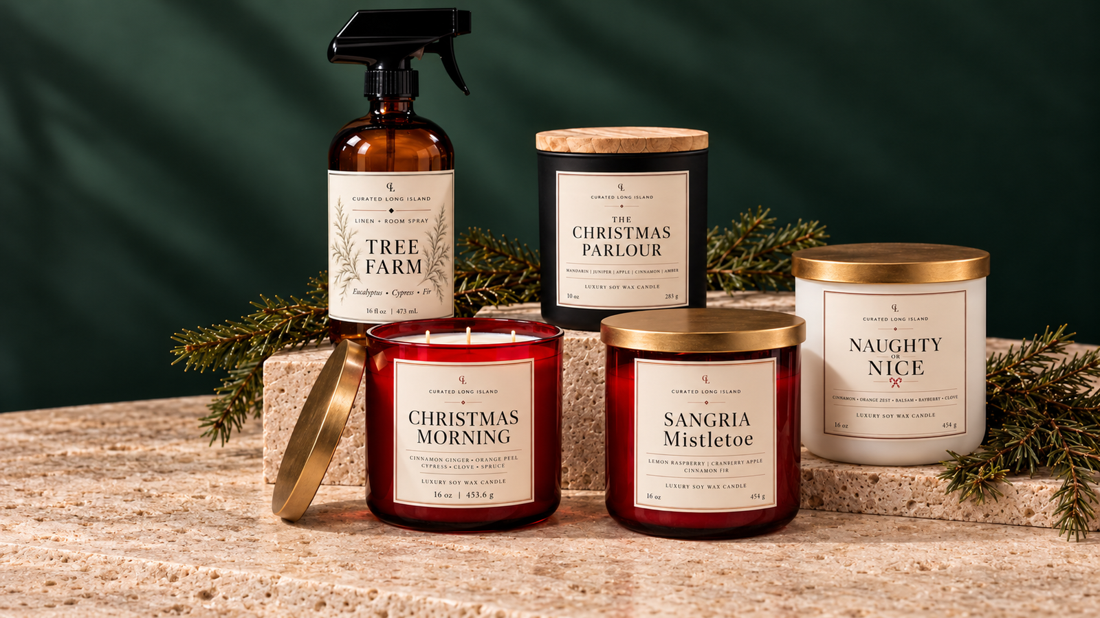 Curated Long Island holiday lineup: Tree Farm room spray, The Christmas Parlour, Christmas Morning, Sangria Mistletoe, and Naughty or Nice candles on warm stone with evergreen branches.